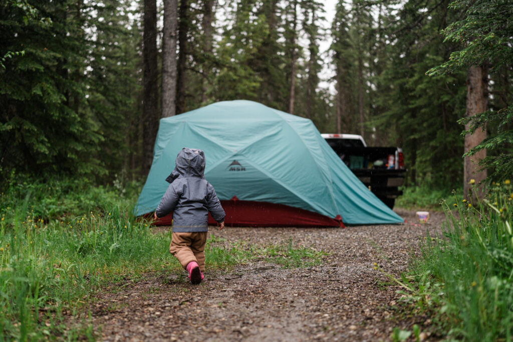 toddler runs towards tent in the rain while car camping
